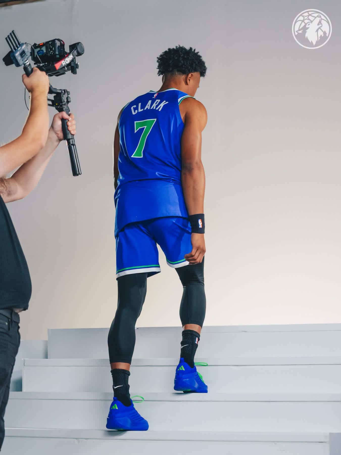 Clark walking up white steps in the blue Wolves #7 uniform as a camera operator films